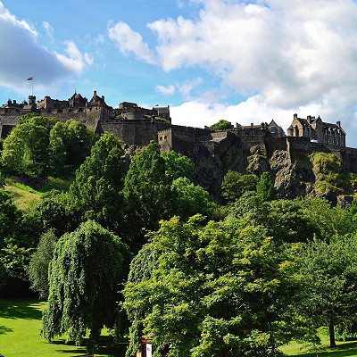 grass and trees in the foregorund looking up to Edinburgh Castle aginst a clear blue sky
